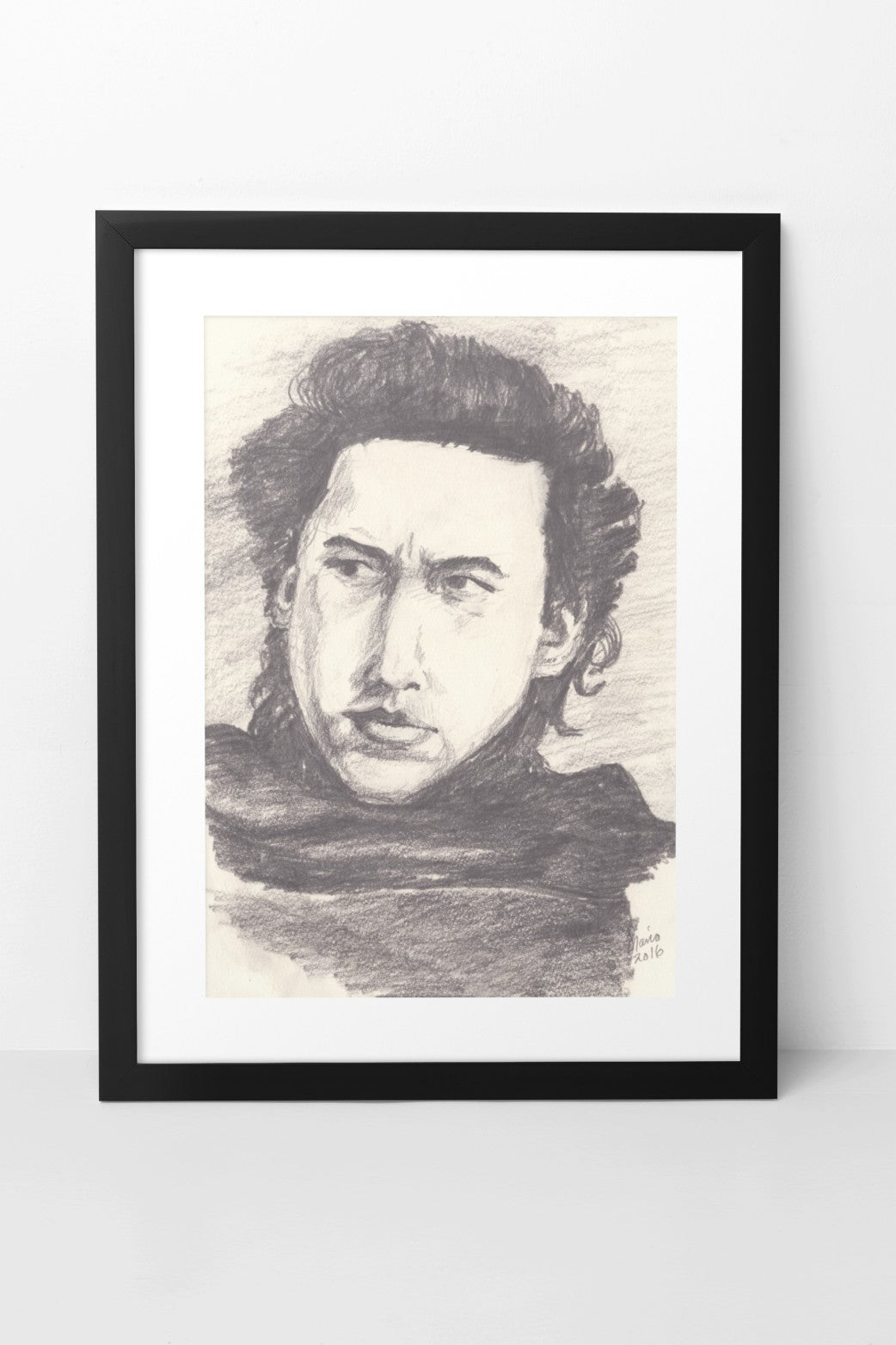 Pencil drawing in grayscale featuring Adam Driver as Kylo Ren from Star Wars. The A4-sized artwork shows a close-up of Kylo Ren from the front, with a serious expression as he looks to the left. His thick hair frames his face, and he is wearing a dark cloak. The artwork is displayed in a black mock-up frame against a neutral background, highlighting its detailed shading and intense atmosphere.