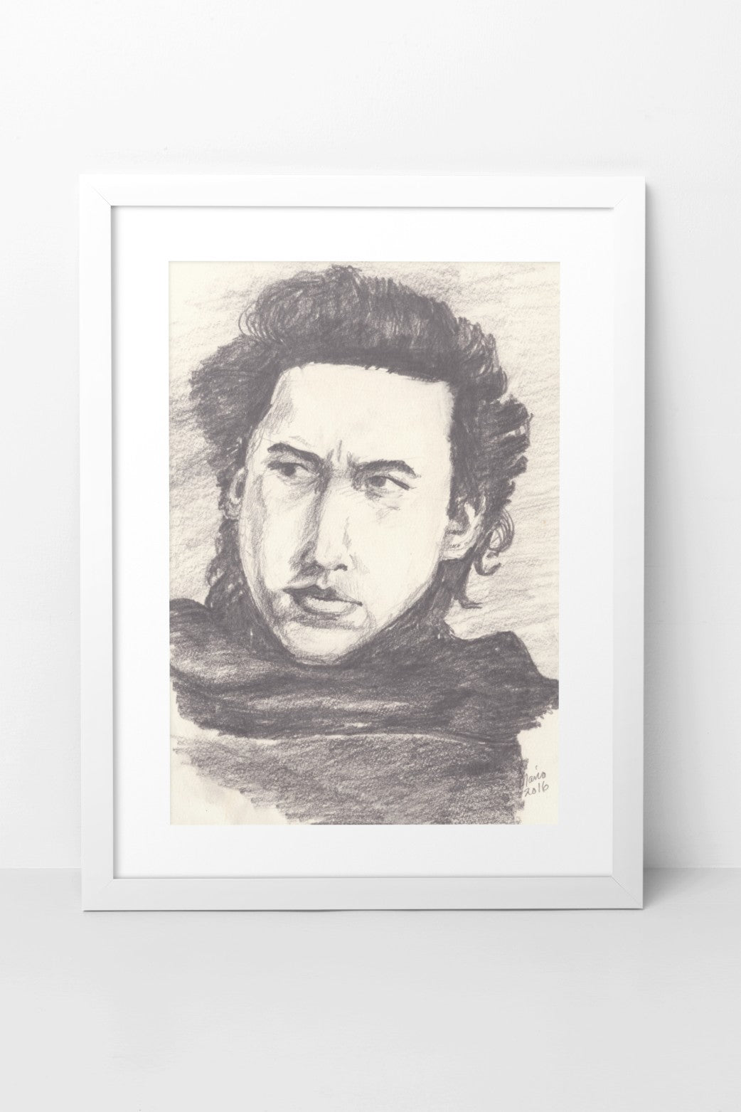 Pencil drawing in grayscale featuring Adam Driver as Kylo Ren from Star Wars. The A4-sized artwork shows a close-up of Kylo Ren from the front, with a serious expression as he looks to the left. His thick hair frames his face, and he is wearing a dark cloak. The artwork is displayed in a white mock-up frame against a neutral background, highlighting its detailed shading and intense atmosphere.