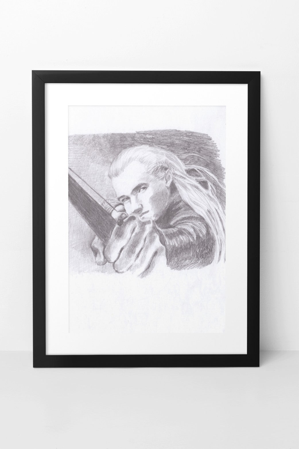 Pencil drawing in grayscale featuring Orlando Bloom as Legolas from The Lord of the Rings. The artwork shows a close-up of Legolas from the front, with his hand outstretched as he draws a bow and arrow. His hair flows gently in the wind, adding a sense of movement to the piece. The artwork is displayed in a black mock-up frame against a neutral background, emphasizing the detailed shading and dynamic composition.