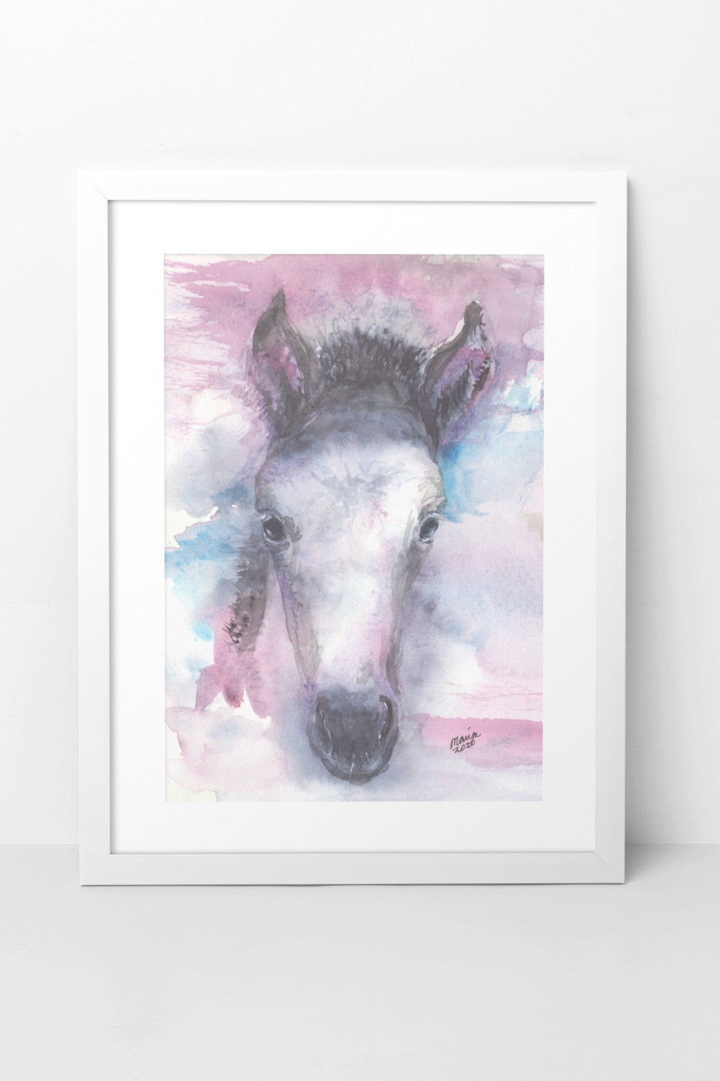 Watercolor painting of a pretty foal, depicted in soft colors with a close-up of its face. The foal has a dark mane, perky ears, and is primarily white. The colors used are a mix of pink, blue, black, and white, creating a delicate and gentle image. The A4-sized artwork is shown in a white mock-up frame against a neutral background, highlighting its soft and serene qualities.