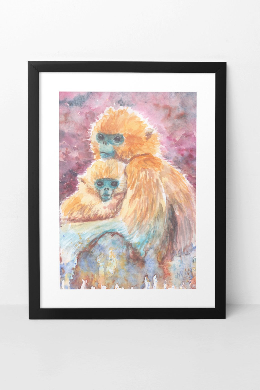 Watercolor painting of a golden snub-nosed monkey mother caressing her baby. The piece is vibrant, showcasing their golden fur, blue faces, deep dark eyes, and subtle smiles. The background features fluid red and black hues at the top, transitioning to green, blue, and brown at the bottom. Titled 'Happy Mother's Day,' the artwork celebrates all types of mothers in the world. The A4-sized artwork is displayed in a black mock-up frame against a neutral background, highlighting its rich colors & tender nature
